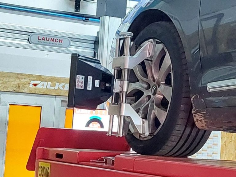 Taller neumáticos Buenas Ruedas Murcia equipamiento profesional Servicio montaje ruedas equilibrado Murcia Coche gris aparcado cerca de un neumático de alto rendimiento con etiqueta visible.